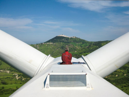 Prüfung Windkraftanlage WEA Stephan Glocker energieprofile Memmingen sitzend auf Windrad mit Blick auf Bergdorf